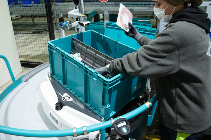 A woman wearing a mask is loading a crate into a Skypod autonomous mobile robot.