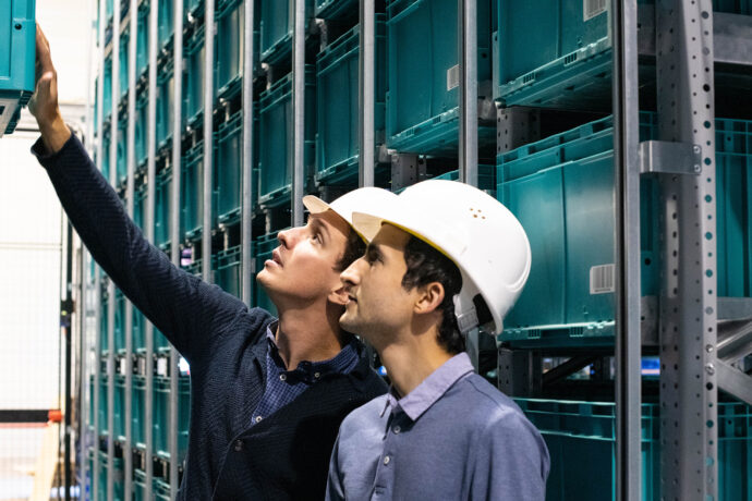 Two men in hard hats looking at shelves in a warehouse.