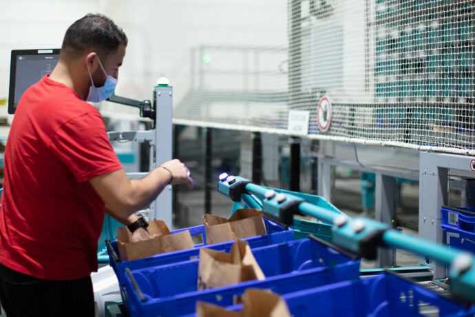 A man with a face mask operating Exotec's Put-to-Light system in a warehouse.