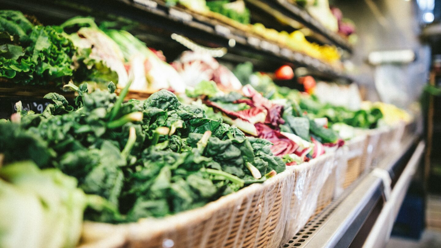 Many baskets of vegetables are on display in a grocery store.