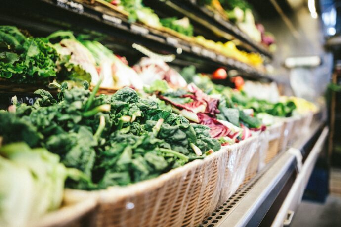 Many baskets of vegetables are on display in a grocery store.