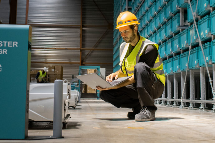 A man working in an industrial warehouse with a laptop managing distribution fulfillment services.