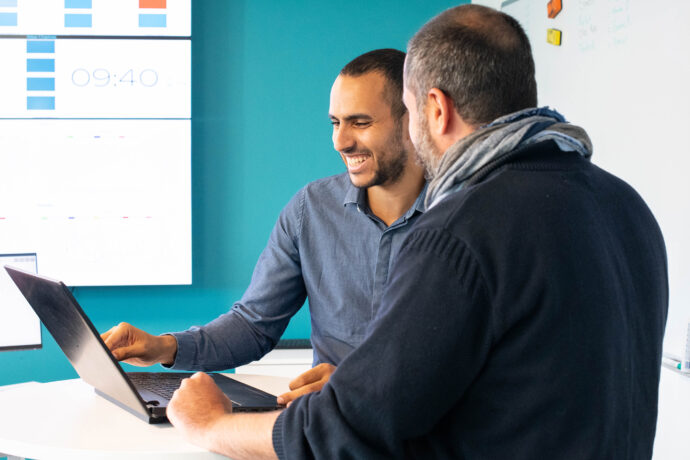 Two men at a desk looking at a laptop.