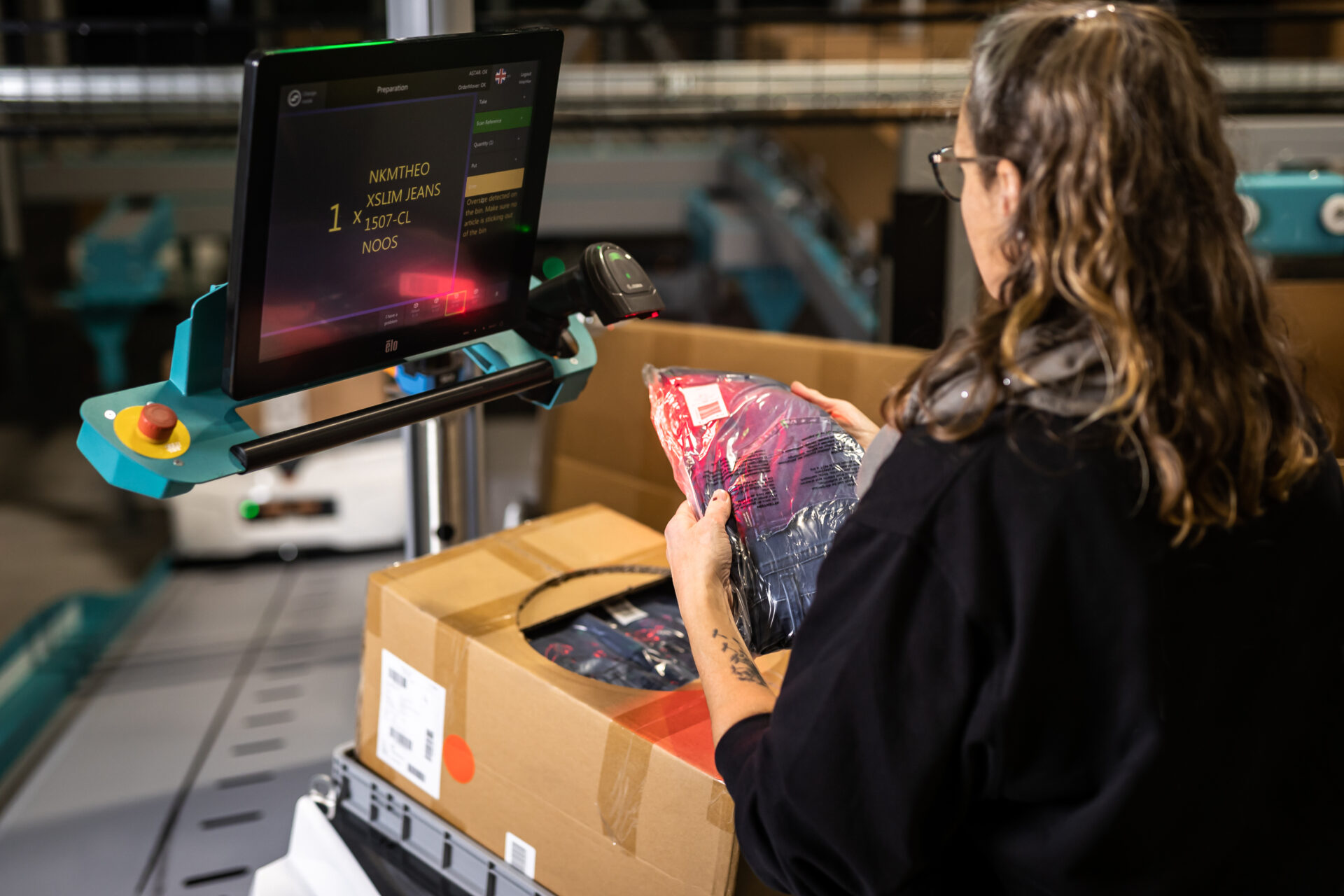 Kommissionierin legt eine verpackte Jeans in einen Karton.